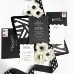 Black and white wedding invitation suite with geometric patterns, white anemone flowers, and polka dot ribbon