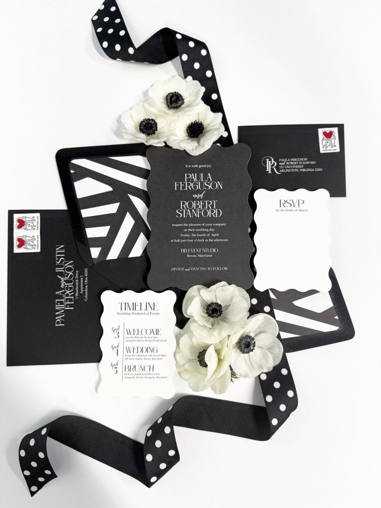 Black and white wedding invitation suite with geometric patterns, white anemone flowers, and polka dot ribbon