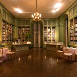 Intimate library event space with green paneled walls, built-in bookshelves, and small cocktail tables