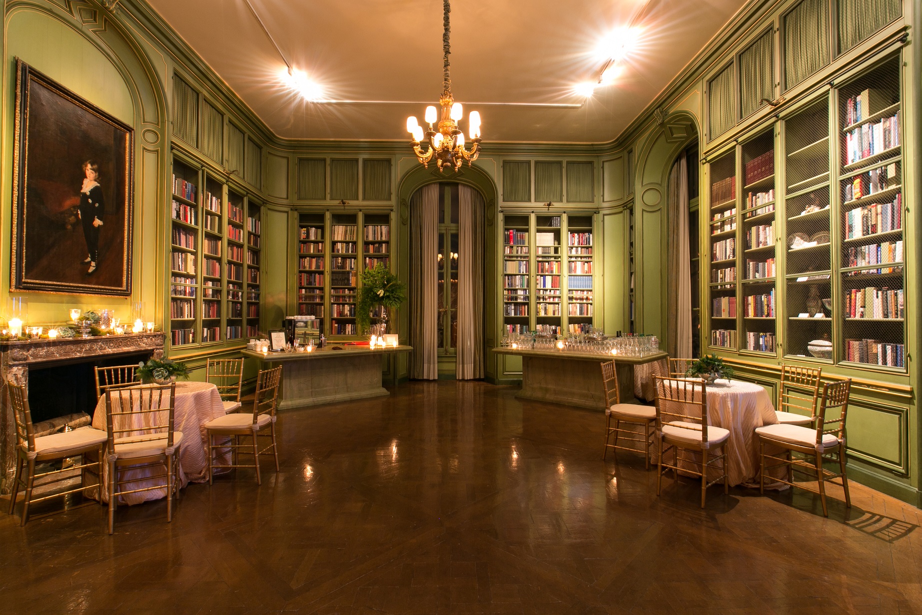 Intimate library event space with green paneled walls, built-in bookshelves, and small cocktail tables
