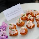 Golden fried canapés topped with pink seafood mousse and fresh herbs, garnished with purple flowers
