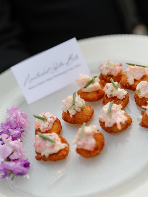 Golden fried canapés topped with pink seafood mousse and fresh herbs, garnished with purple flowers