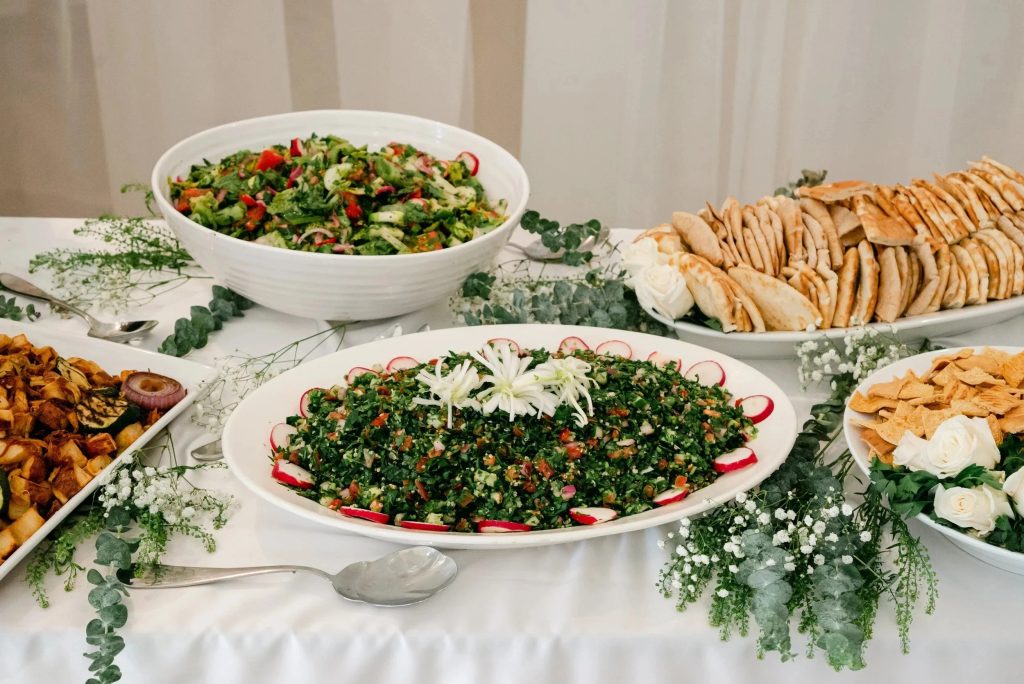 Wedding catering spread featuring fresh salads, pita bread, and Mediterranean dishes with floral accents