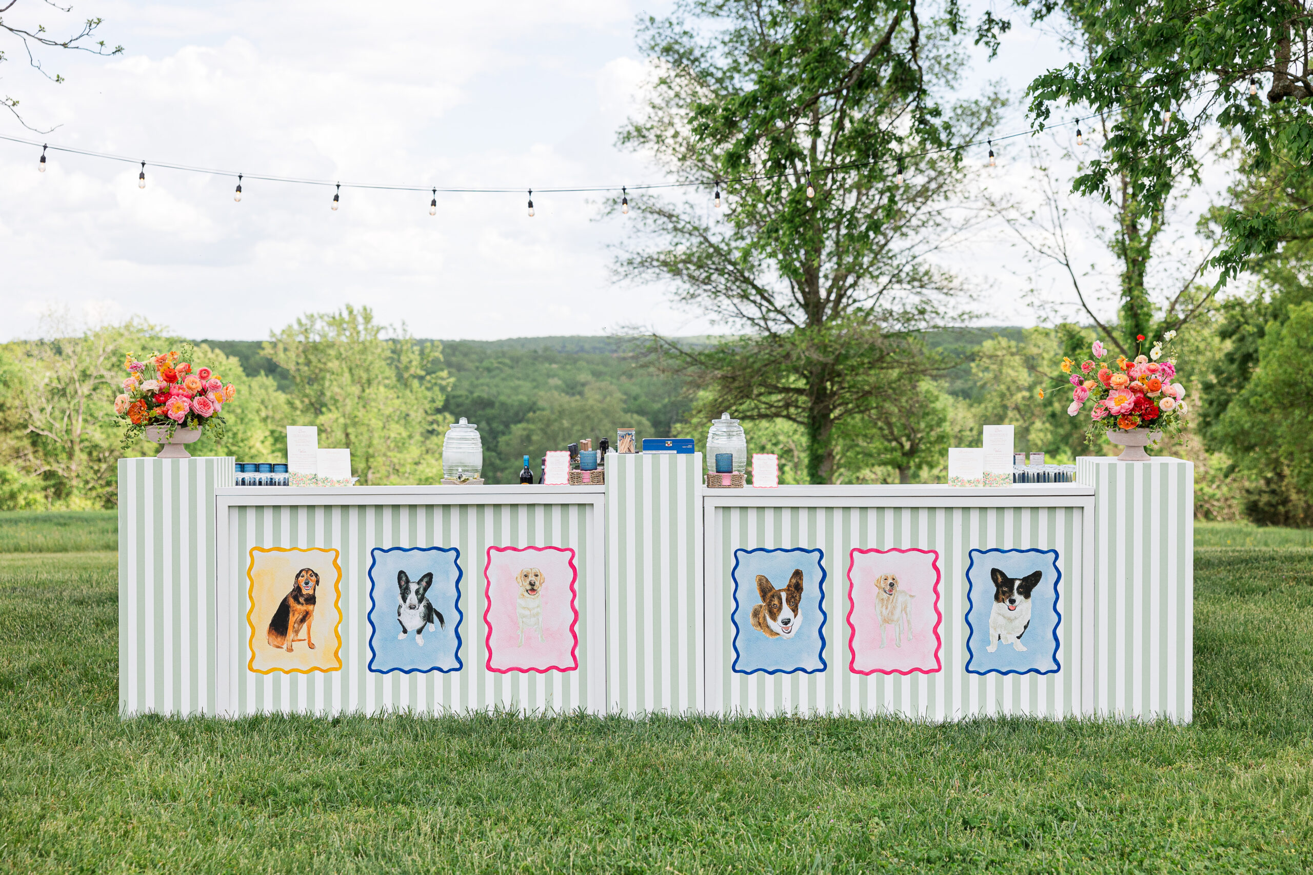 Two striped bar stations with dog portrait decorations, vibrant floral arrangements, and beverage dispensers in outdoor garden setting