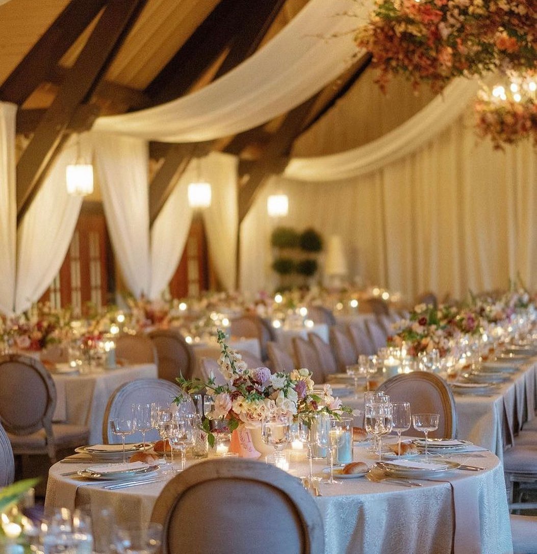 Elegant ballroom reception with draped fabric ceiling, exposed beams, round tables with floral centerpieces and candlelight