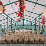 Wedding reception tent with green framework, bougainvillea garlands, floral ceiling medallion, and long dining table