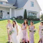 Bridal party in mauve dresses walking together on lawn in front of contemporary white barn venue