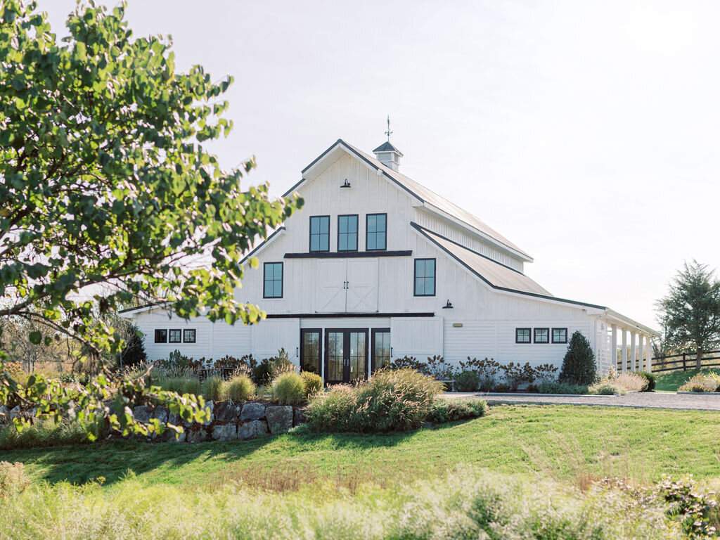 White barn-style wedding venue with cupola and black-trimmed windows surrounded by landscaped grounds in Northern Virginia