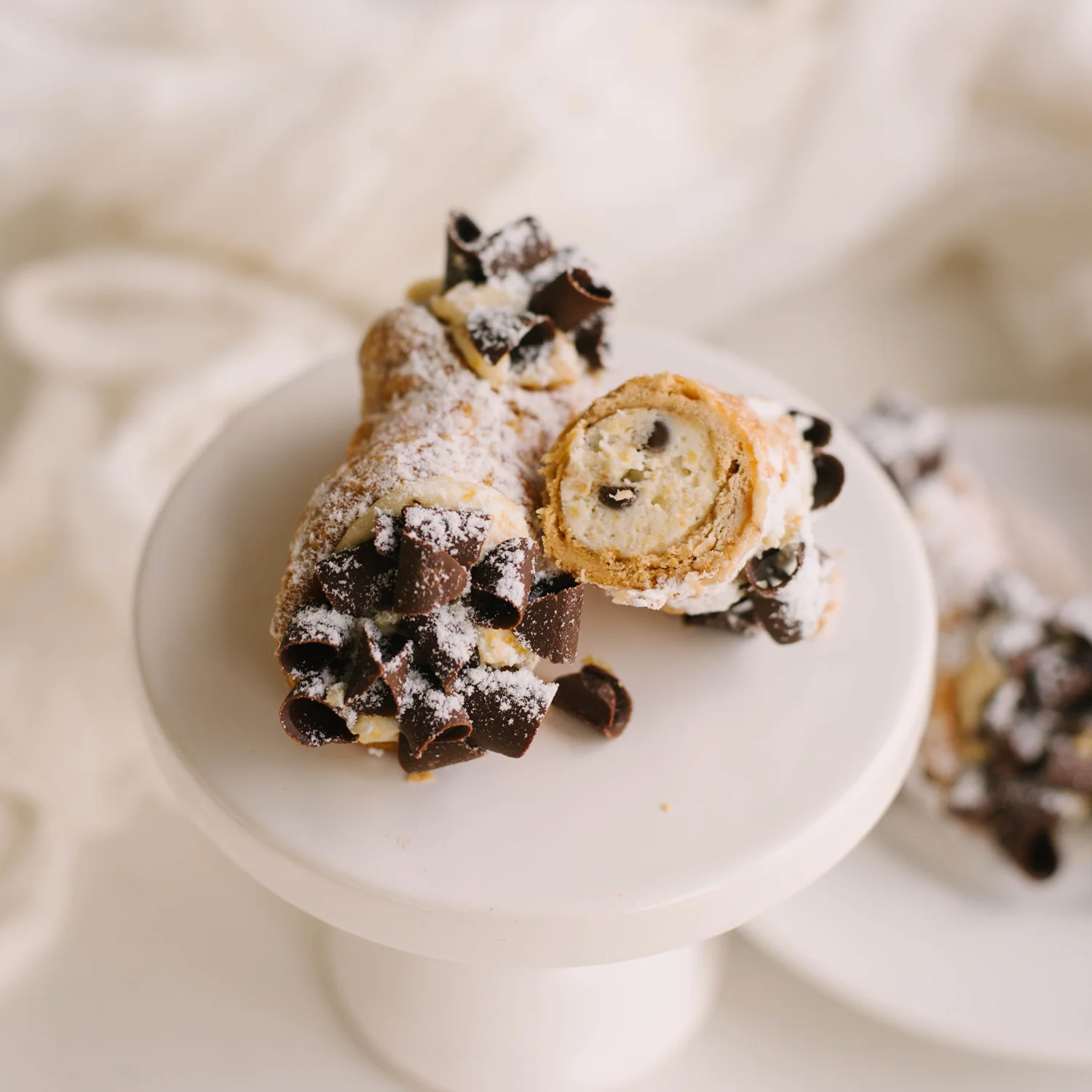 Chocolate chip cannoli dusted with powdered sugar on white cake stand