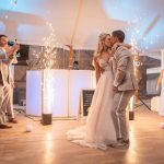 Bride and groom sharing first dance kiss surrounded by sparkler fountains and wedding guests under tent