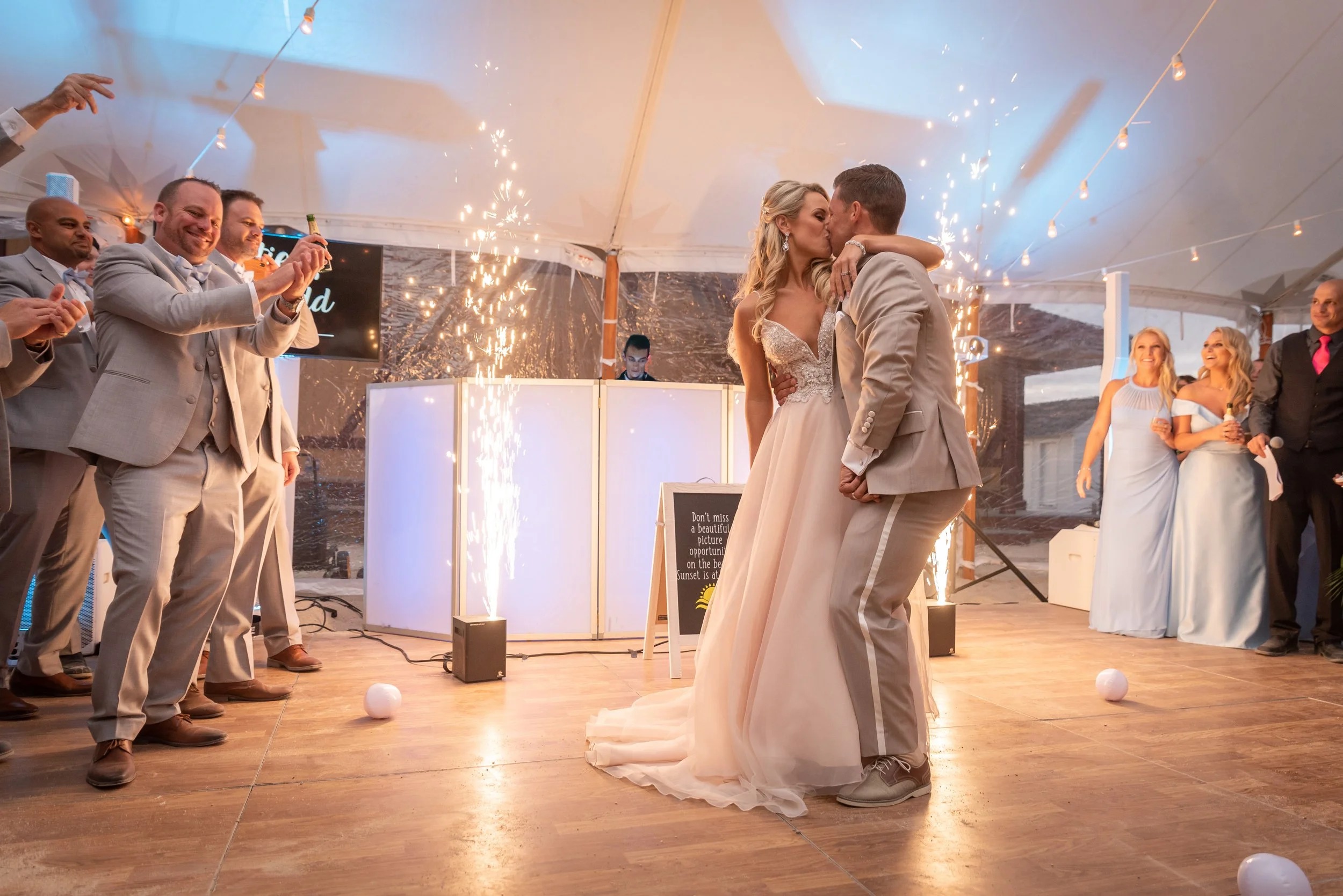 Bride and groom sharing first dance kiss surrounded by sparkler fountains and wedding guests under tent
