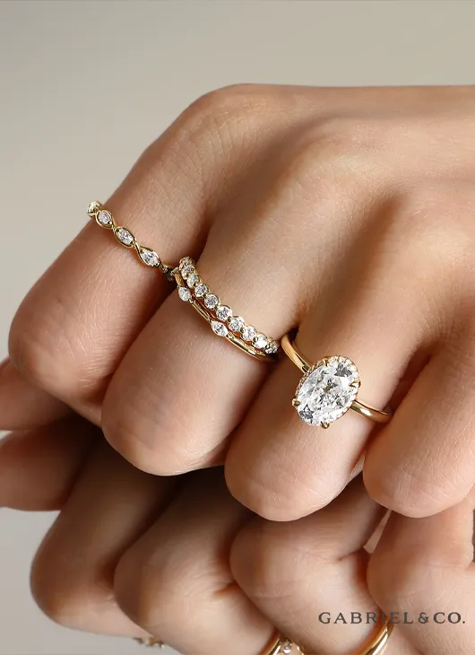 Hand wearing emerald-cut diamond solitaire engagement ring with delicate pavé wedding band