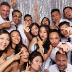 Wedding guests making peace signs and silly faces in photo booth with silver sequin backdrop