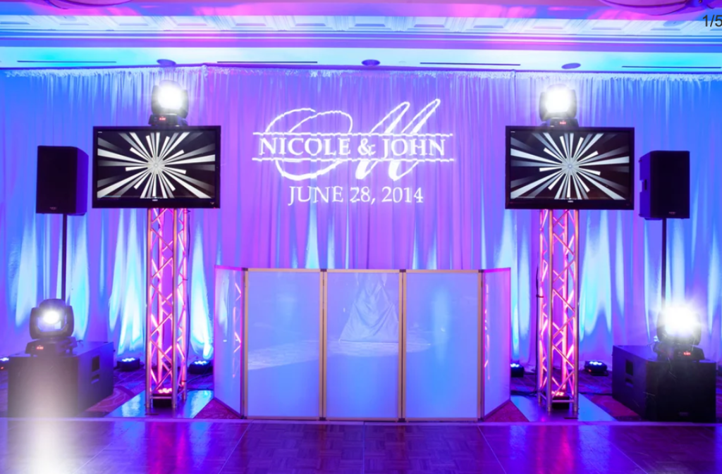 Professional DJ setup with custom monogram lighting, purple uplighting, speakers, and illuminated booth for Nicole & John wedding
