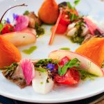 Artfully plated appetizer with seared tuna, poached pear, watermelon radish, and edible flowers