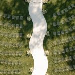 Bird's eye view of outdoor wedding ceremony layout with white fabric aisle and floral accent arrangements