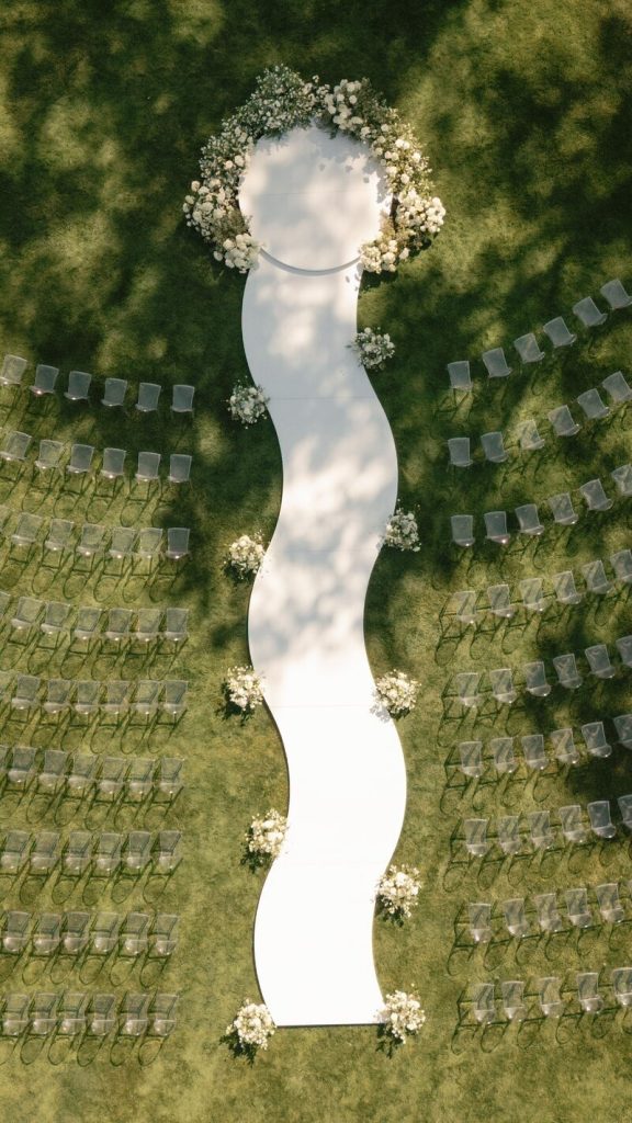 Bird's eye view of outdoor wedding ceremony layout with white fabric aisle and floral accent arrangements