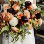 Bridal bouquet with peach roses, white dahlias, burgundy scabiosa, and cascading eucalyptus and ferns