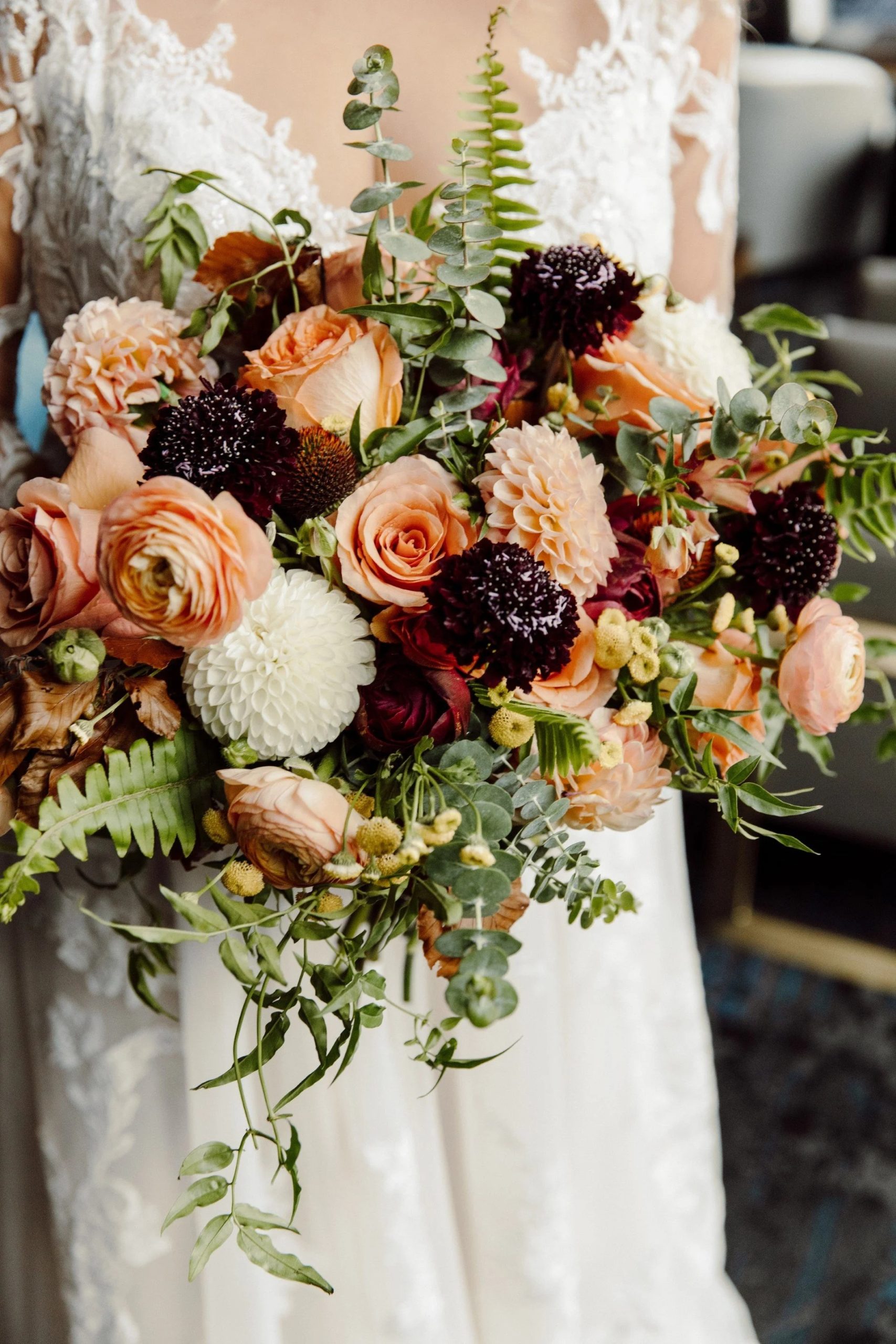 Bridal bouquet with peach roses, white dahlias, burgundy scabiosa, and cascading eucalyptus and ferns