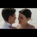 Newlyweds embracing on a beach with pearl necklace and ocean backdrop