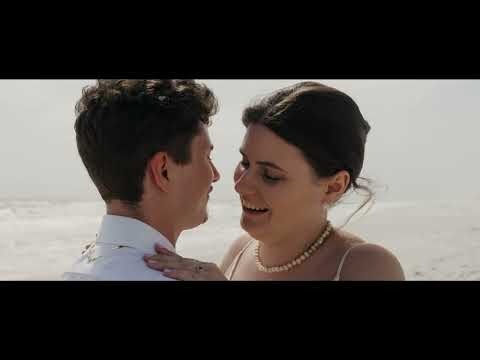 Newlyweds embracing on a beach with pearl necklace and ocean backdrop