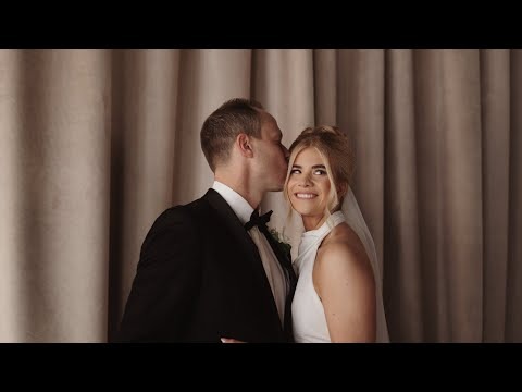 Groom kissing bride's temple as she smiles at camera in elegant indoor setting