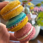 Hand holding colorful macaron tower with sparkly yellow, turquoise, and pink cookies decorated with pearl sprinkles