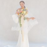 Bride in flowing white gown holding colorful wedding bouquet with pink, orange, and yellow flowers