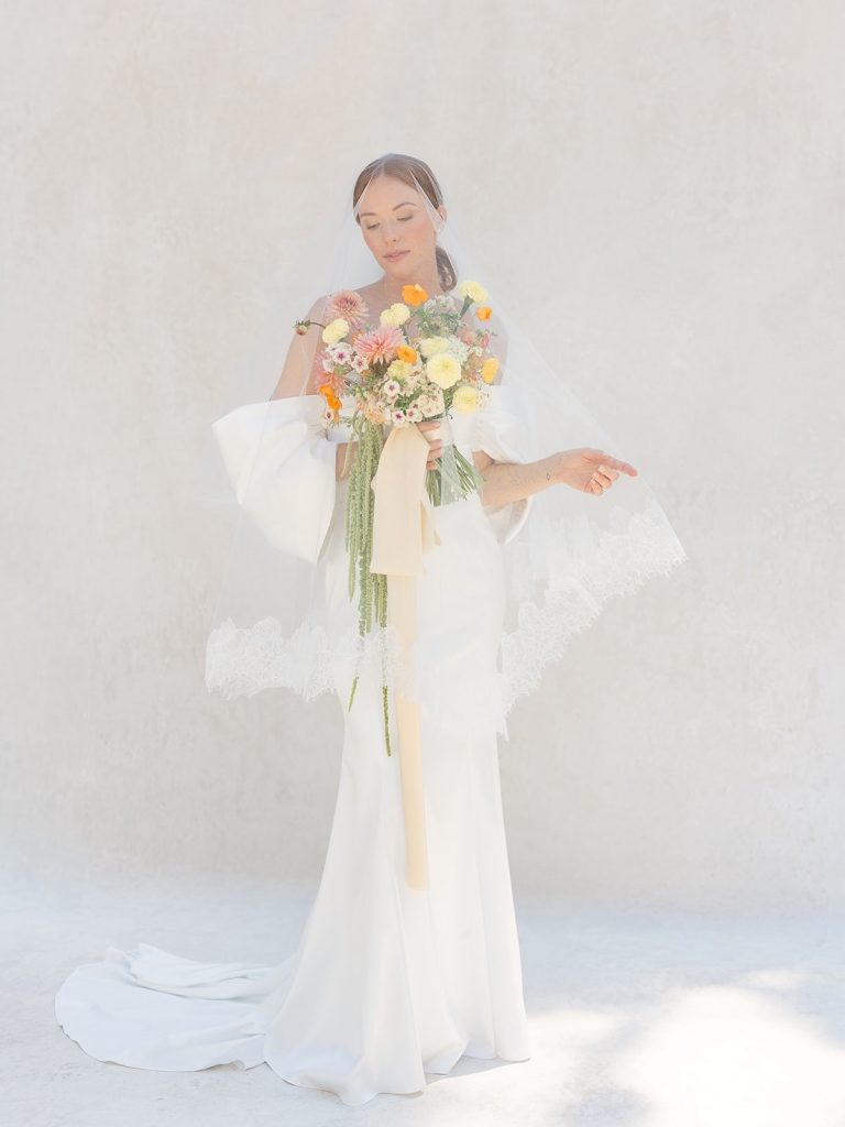 Bride in flowing white gown holding colorful wedding bouquet with pink, orange, and yellow flowers