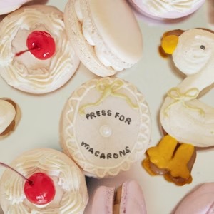 Assorted macarons with cherry centers and branded cookie reading "Press for Macarons" surrounded by bear-shaped cookies