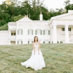 Bride in flowing white ball gown standing on lawn in front of white colonial-style estate venue