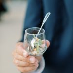 Guest in navy suit holding glass with seafood appetizer and cocktail spoon