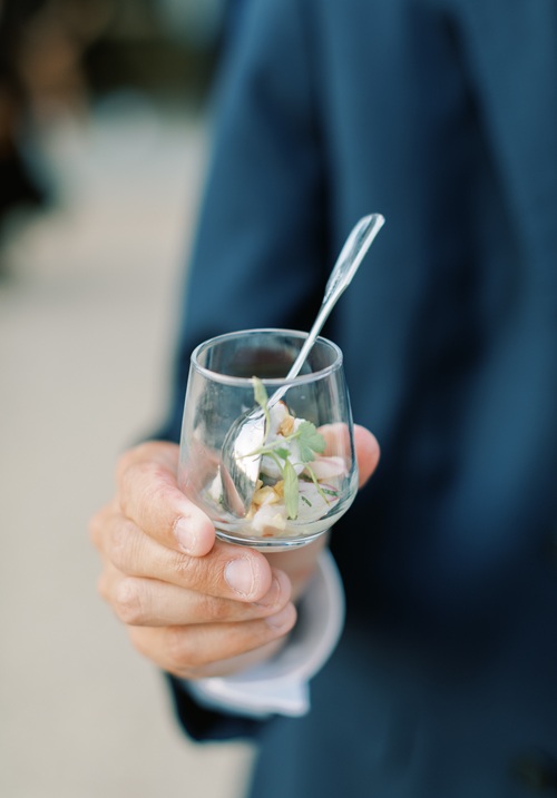 Guest in navy suit holding glass with seafood appetizer and cocktail spoon