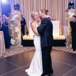 Bride and groom embracing during first dance with dramatic stage lighting and floral decor