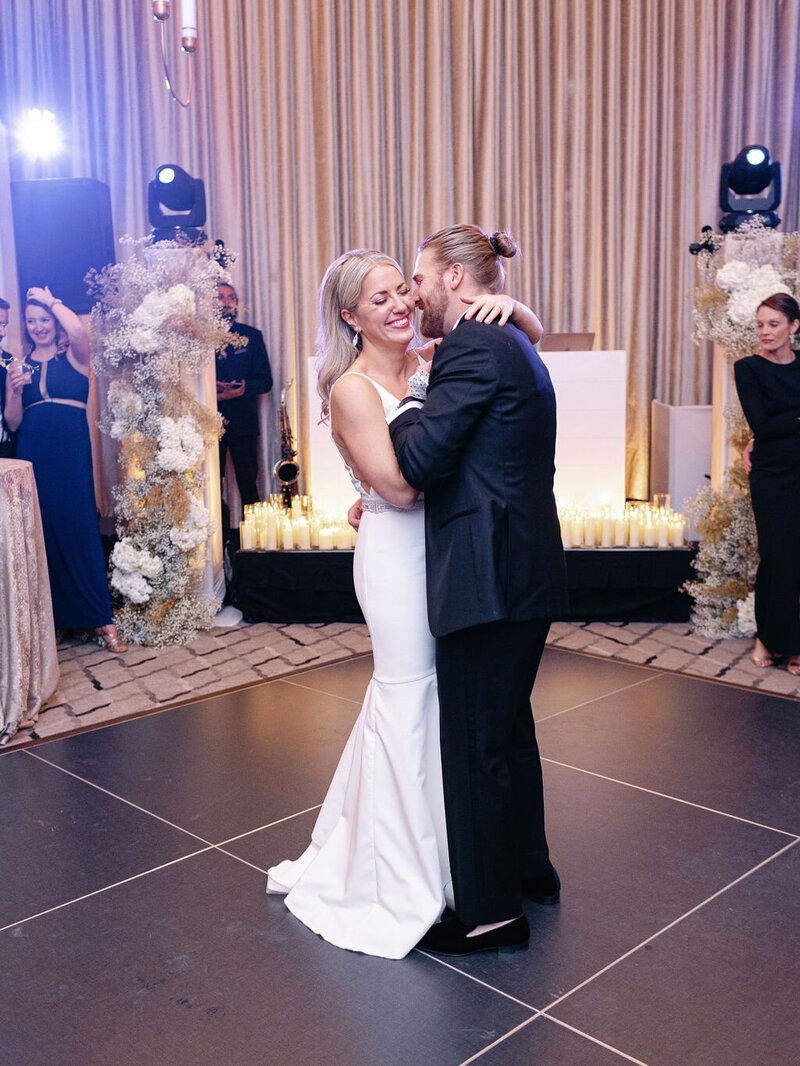 Bride and groom embracing during first dance with dramatic stage lighting and floral decor