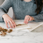 Calligrapher arranging wedding invitations with gold calligraphy and silk ribbon on marble surface