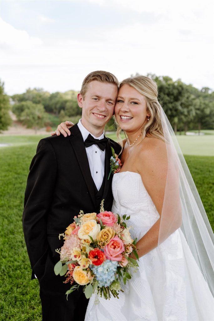 Smiling couple in formal wedding attire holding colorful spring bouquet outdoors