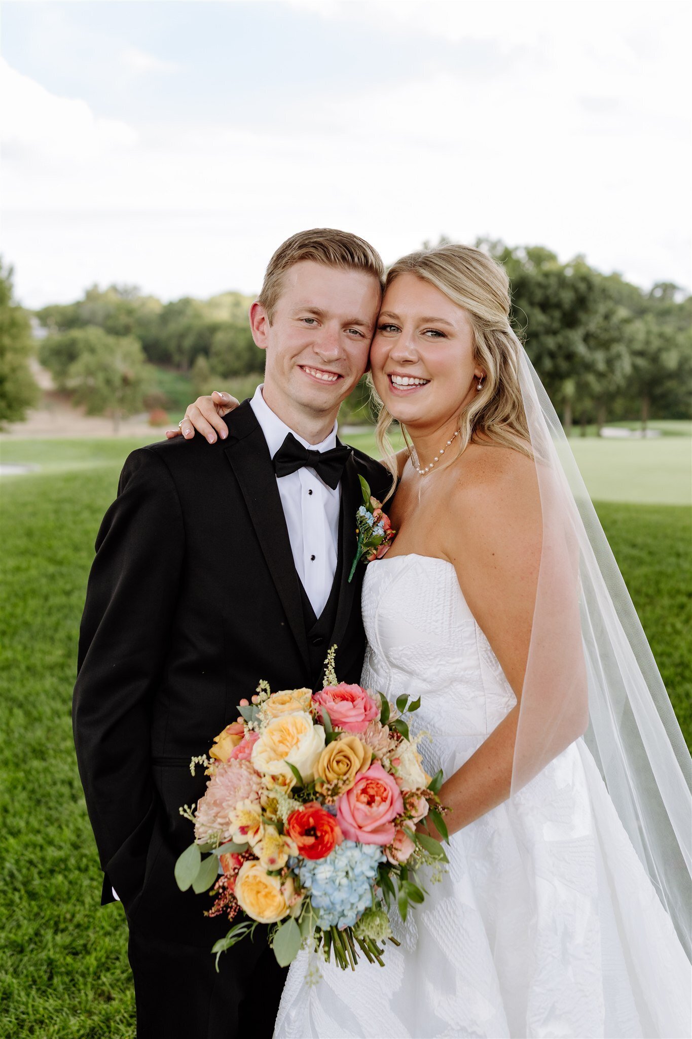 Smiling couple in formal wedding attire holding colorful spring bouquet outdoors