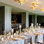 Wedding reception with geometric chandeliers, blue linens, and candlelit tables in sage green room