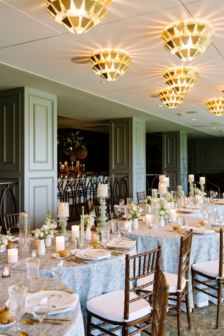 Wedding reception with geometric chandeliers, blue linens, and candlelit tables in sage green room