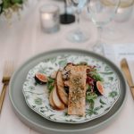 Plated chicken breast with roasted vegetables and greens served on speckled ceramic plate with rose gold flatware
