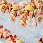 Cooked crab claws arranged on parchment paper with lemon wedges