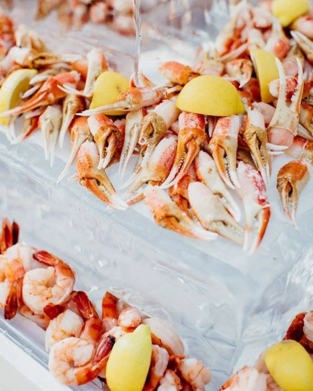 Cooked crab claws arranged on parchment paper with lemon wedges