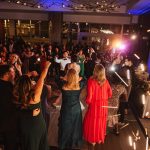 Wedding guests dancing at upscale reception venue with dramatic lighting and floor-to-ceiling windows