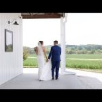 Newlyweds holding hands while walking through white barn doors overlooking rural Nebraska landscape