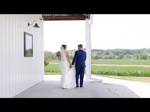 Newlyweds holding hands while walking through white barn doors overlooking rural Nebraska landscape