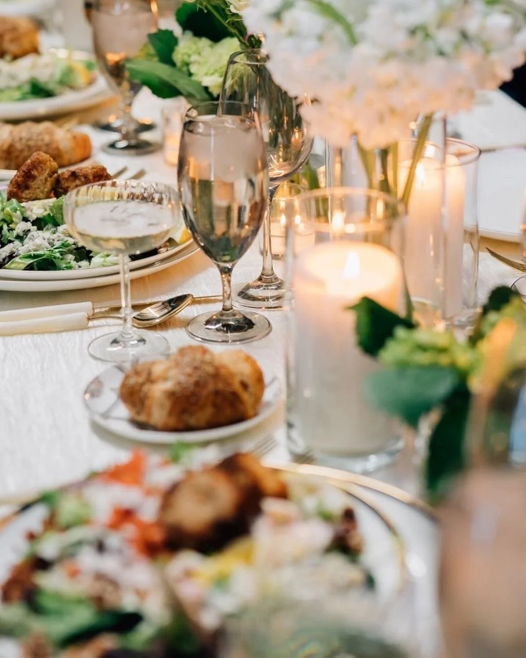 Wedding reception table with salads, rolls, wine glasses, and candlelight