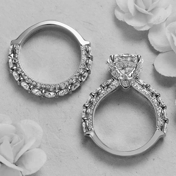 Platinum engagement ring with cushion-cut diamond and ornate baguette-accented band alongside matching wedding band with white roses