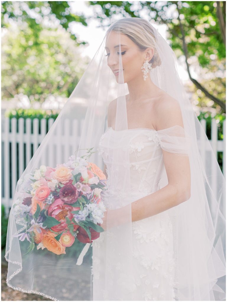 Bride in off-shoulder gown and veil holding colorful bouquet outdoors