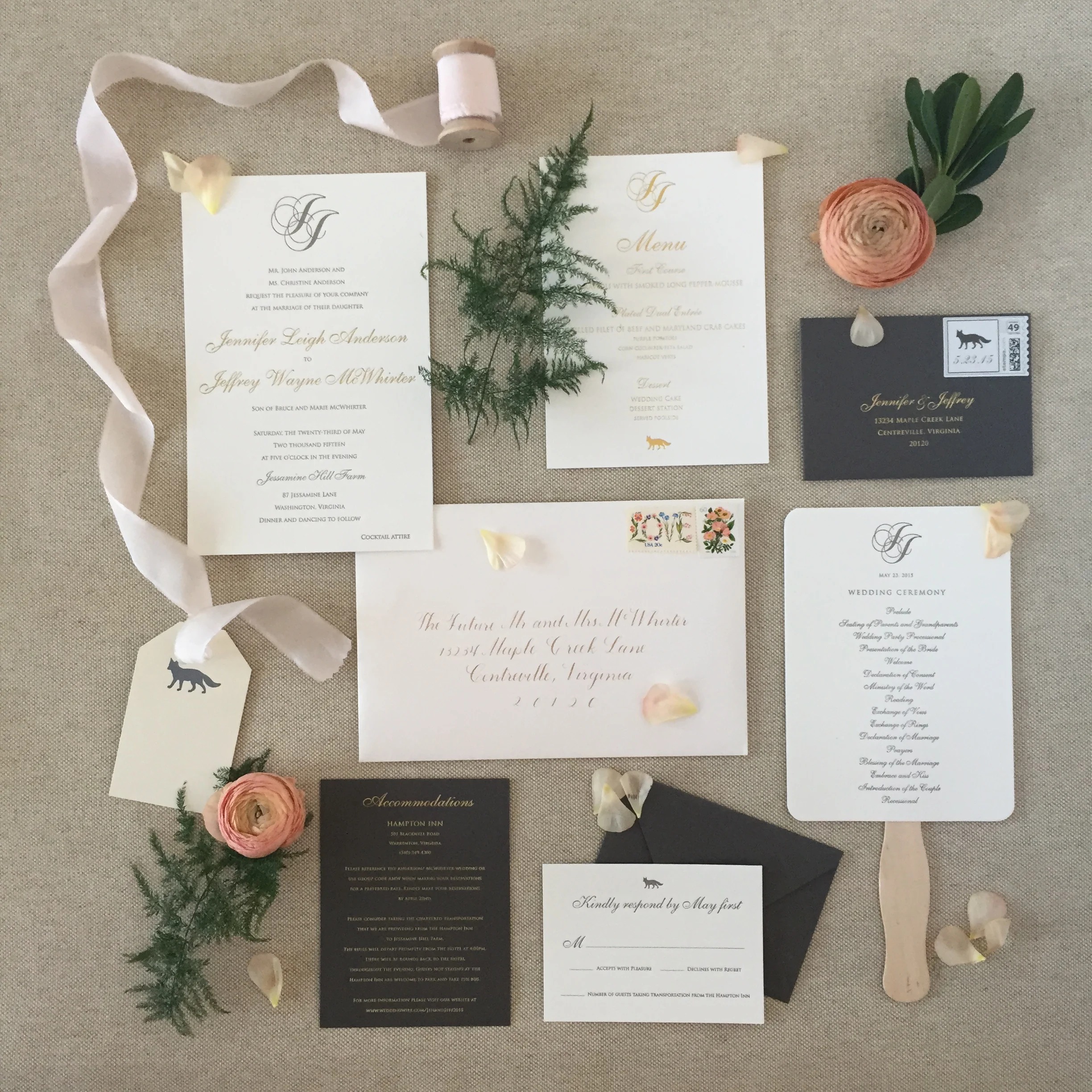 Elegant wedding invitation suite with gold calligraphy, charcoal gray envelopes, coral ranunculus, evergreen sprigs, and fox motif details on burlap background